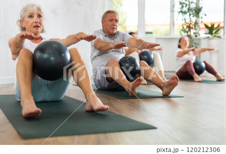 Portrait of elderly people doing exercises for press with pilates ball during group class in fitness studio 120212306