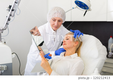 Elderly female cosmetician showing results of facial procedure to smiling woman Elderly female cosmetician showing results of facial procedure to smiling woman 120212413