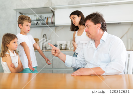 At home in kitchen, outraged mom and dad scold their son and daughter for disobedience. 120212621