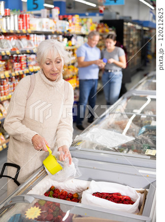 Aged woman filling plastic bag with frozen peppers in store 120212625
