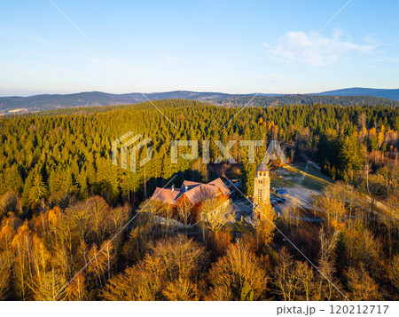 A sunny autumn morning reveals the Bramberk lookout tower and hut nestled in the Jizera Mountains, surrounded by vibrant foliage and serene landscapes. 120212717