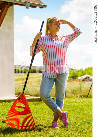 Woman using rake to clean up garden 120212786