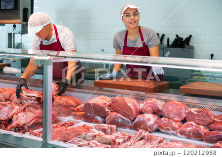 In butcher shop, young female vendor in uniform apron, gloves, cap holds cutting board In butcher shop, young female vendor in uniform apron, gloves, cap holds cutting board 120212988