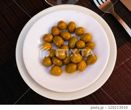On white plate lies portion of large ripe green olives with stone. 120213010