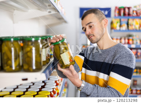 In Russian goods store, man choose jar of pickled cucumbers 120213298