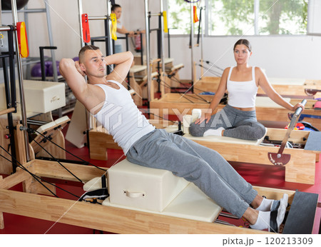 Young guy doing press exercises on reformer device 120213309