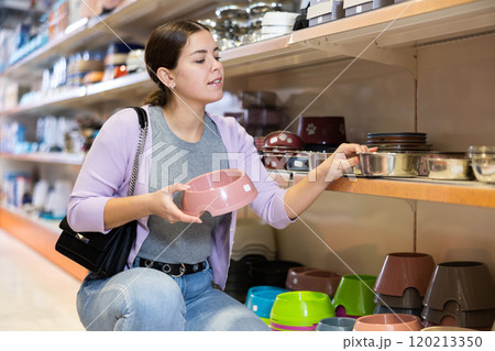 Young woman choosing bowl for puppy in pet supplies store 120213350