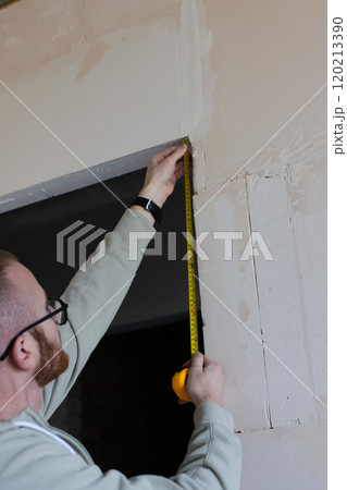 Man with measuring tape measuring doorway. Beginning of renovation work in a house. 120213390
