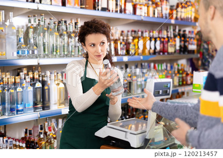 Woman seller near a cash register offers to buy a bottle of vodka to man Woman seller near a cash register offers to buy a bottle of vodka to man 120213457
