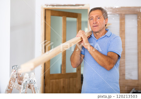 Middle-aged male carpenter in uniform holding wooden planks indoors 120213503