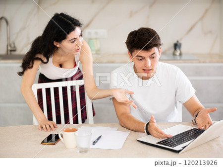 Sad freelancer husband works at home on laptop and listens to her wife reproaches in frustration. 120213926