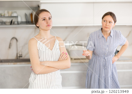 Offended young girl standing in the kitchen, angry mother talking Offended young girl standing in the kitchen, angry mother talking 120213949