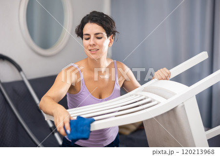 Latino woman doing cleaning in the room - dusting chair 120213968