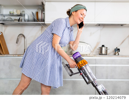 Housewife is cleaning the room - vacuuming and talking on smartphone at same time 120214079