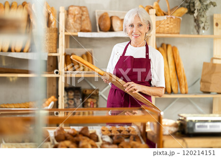 Mature woman entrepreneur, owner of baker puts baguettes in paper bag. 120214151