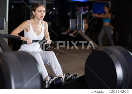 Girl performs exercises with rowing machine in gym 120214206