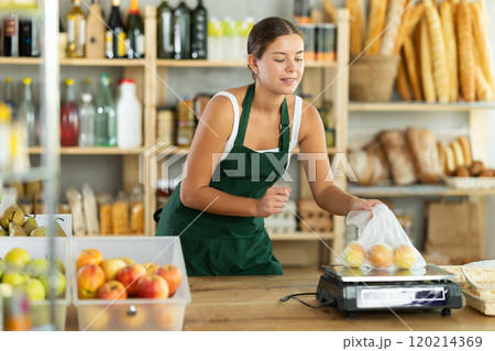 Young woman seller weighs apples in bag 120214369