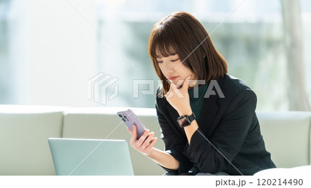 パソコンとスマホを使って真剣な表情で考える女性・ビジネスウーマン 120214490