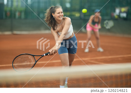 Girl swinging racket to hit ball during tennis doubles on outdoor court 120214821