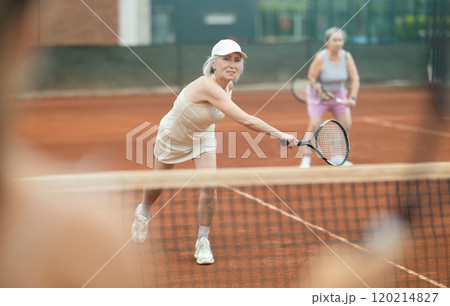 Aged woman swinging racket during doubles tennis match on outdoor court 120214827