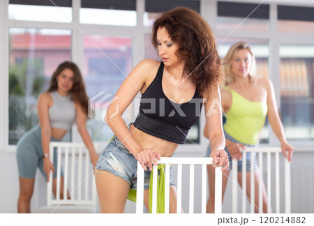 Group of women in high heels rehearsing dance while leaning on chair Group of women in high heels rehearsing dance while leaning on chair 120214882
