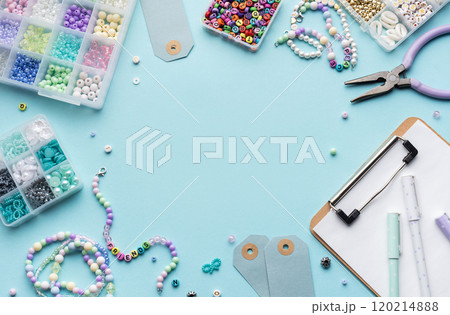 Colorful beads, pliers, clipboard and price tags arranged on blue surface for diy bracelet making 120214888