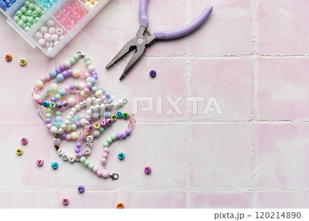 Colorful beads and jewelry making tools arranged on pink tile surface 120214890