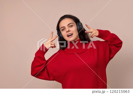 Happy woman wearing red sweater and headphones enjoying listening music on pink background. 120215063