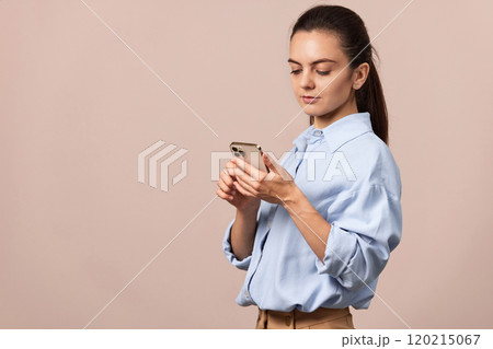 positive pretty woman using mobile phone looking at smartphone on beige background. copy space positive pretty woman using mobile phone looking at smartphone on beige background. copy space 120215067