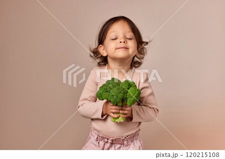 cute little child girl holding fresh green raw broccoli on beige background. healthy baby food. kid loves vegetables cute little child girl holding fresh green raw broccoli on beige background. healthy baby food. kid loves vegetables 120215108