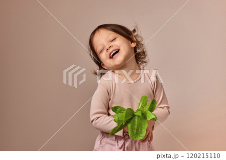 cute child girl holding fresh green salad on beige background. healthy baby food. 120215110