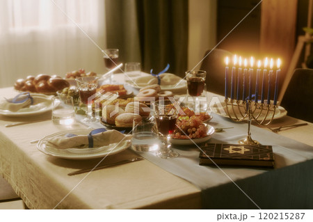 Served table with traditional treats, lit candles and Torah on table top in dining room 120215287