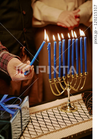 High angle shot of unrecognizable man and woman standing next to table with golden candlestick, gift and book while lighting candle up 120215317