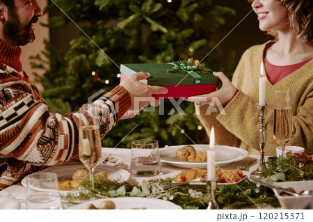 Medium close up of beloved wife and husband exchanging gifts while celebrating X-mas at festive table with huge number of traditional dishes and champagne 120215371