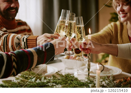 Medium close up of friends sitting at festive table and clinking glasses full of sweet champagne while spending X-mas eve together 120215410