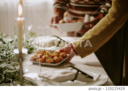 Unrecognizable female hand serving table with plate full of oven roasted potatoes while his husband helping her in blurred background Unrecognizable female hand serving table with plate full of oven roasted potatoes while his husband helping her in blurred background 120215429