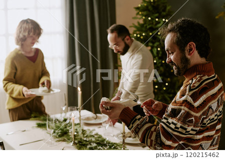 Caucasian family in sweaters serving festive table with luxury tableware while preparing for Christmas evening Caucasian family in sweaters serving festive table with luxury tableware while preparing for Christmas evening 120215462
