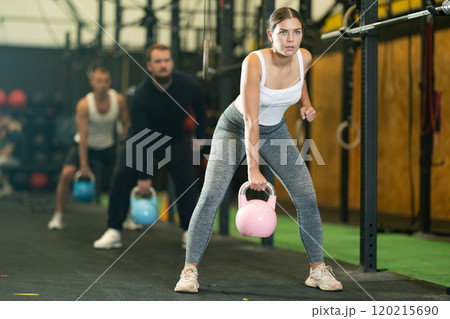 Sportive young woman lifting heavy kettlebell in sports hall Sportive young woman lifting heavy kettlebell in sports hall 120215690
