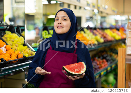 Supermarket seller in hijab and apron offers to buy watermelon 120215758