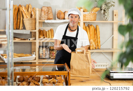 Middle-aged salesman holding paper bag in bakery Middle-aged salesman holding paper bag in bakery 120215792