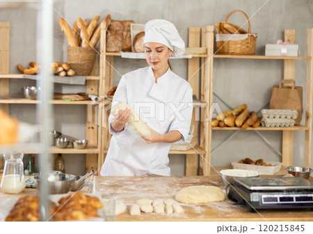 Process of making baguette, loaf or bread in bakery - female baker kneads and rolls dough to give shape of future bread Process of making baguette, loaf or bread in bakery - female baker kneads and rolls dough to give shape of future bread 120215845