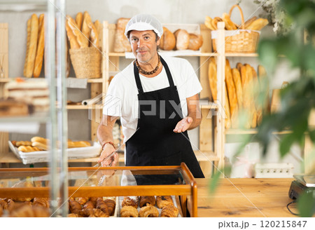 Portrait of friendly baker selling fresh baguettes and croissants in bakery Portrait of friendly baker selling fresh baguettes and croissants in bakery 120215847
