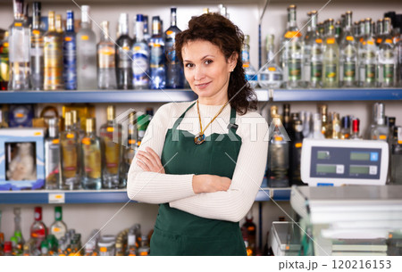 Portrait of positive saleswoman at cash register of liquor store 120216153