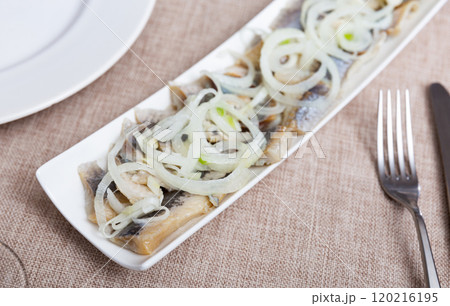 on rectangular plate salted herring fillet cut into pieces with onion rings and sprig of parsley 120216195