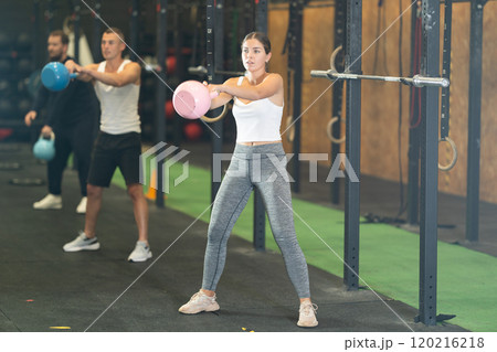 Sportive young woman lifting heavy kettlebell in sports hall Sportive young woman lifting heavy kettlebell in sports hall 120216218