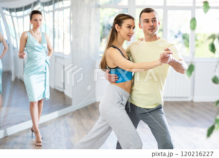 Couple practicing passionate tango guided by female dance instructor in studio Couple practicing passionate tango guided by female dance instructor in studio 120216227