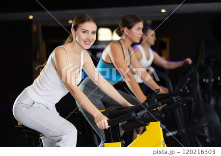 Smiling young girl doing spin bike exercises in well-equipped gym Smiling young girl doing spin bike exercises in well-equipped gym 120216303
