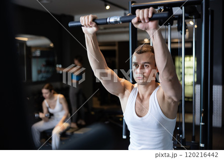 Slender athletic man work out muscles of arms and shoulders on simulator in gym of fitness club 120216442