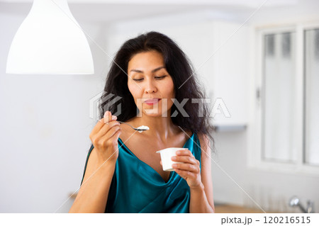 Portrait of positive woman in nightdress eating yogurt at home Portrait of positive woman in nightdress eating yogurt at home 120216515