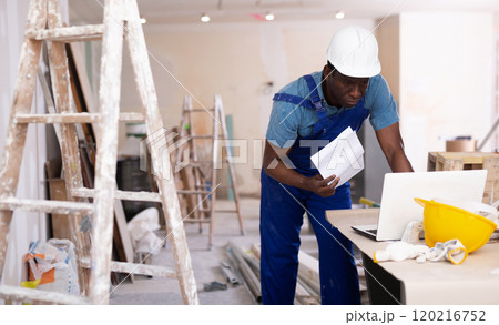 African american civil engineer with drawings in his hands, checks the house reconstruction plan on a laptop African american civil engineer with drawings in his hands, checks the house reconstruction plan on a laptop 120216752